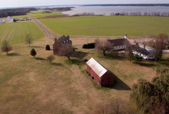 Aerial view of red barn and homestead, farm fields in the background, and open water past the farm fields.