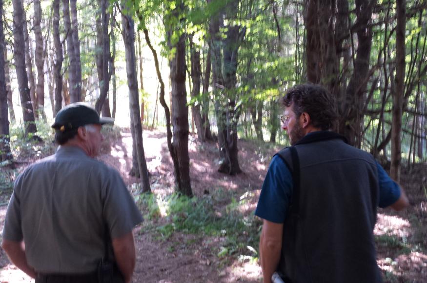 Two land managers, one of which is park staff, discuss forest management in the forest.