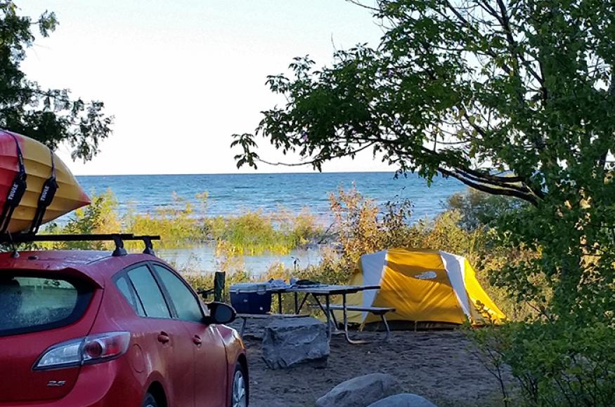 View of waterfront campsite with car, picnic table, and small tent