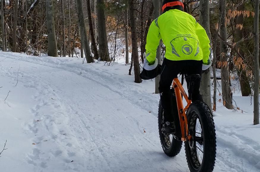 Person in high visibility yellow jacket riding a fat tire on a winter trail